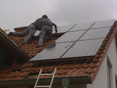 Bild vergrern: zu sehen sind zwei Handwerker, die auf dem Dach Solarmodule anbringen
